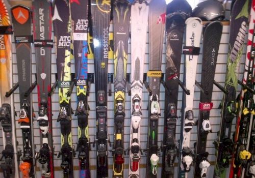 The image shows multiple pairs of skis leaning against a wall with various brands and designs displayed.