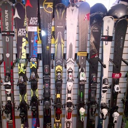 The image shows multiple pairs of skis leaning against a wall with various brands and designs displayed.